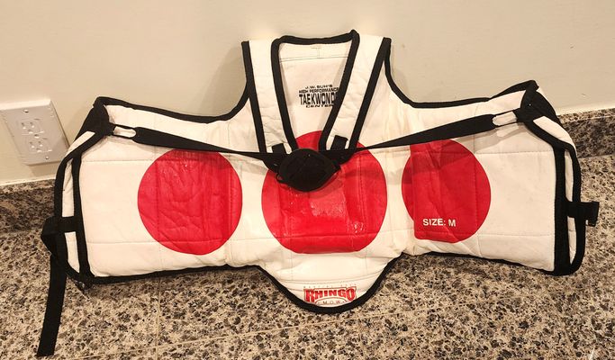 This is a Rhingo Taekwondo chest guard, size me The guard features red circular targets on a white background.